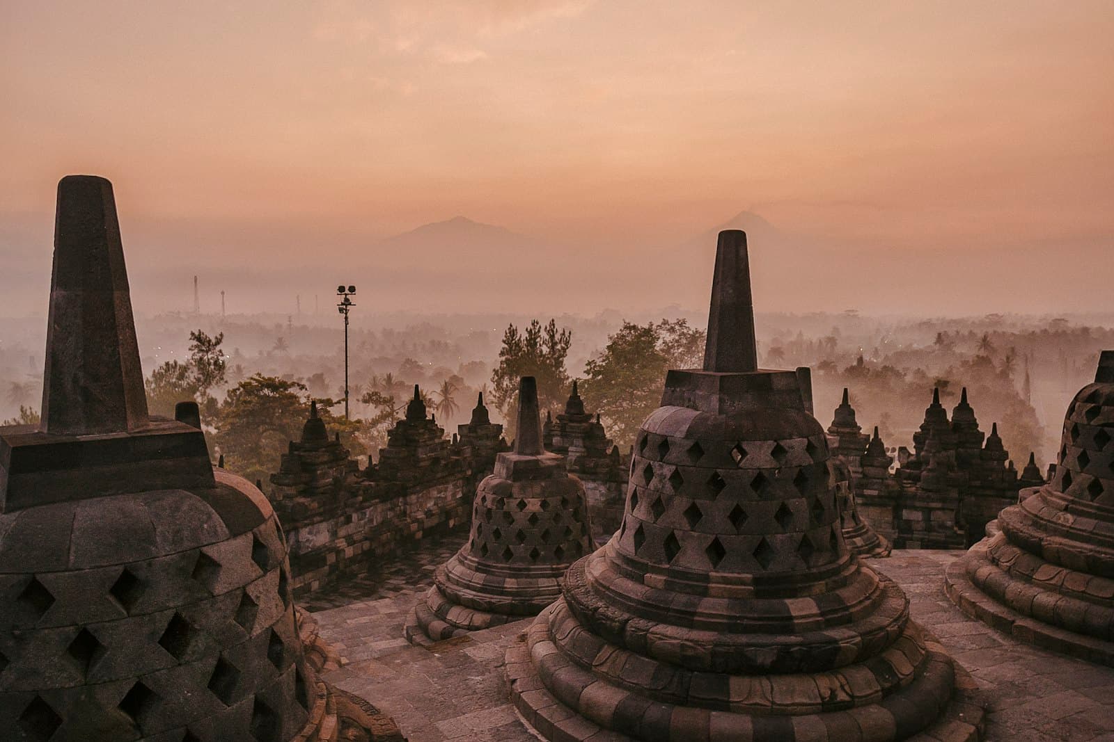 Stone stupas at Borobudur in the morning mist, with mountains behind