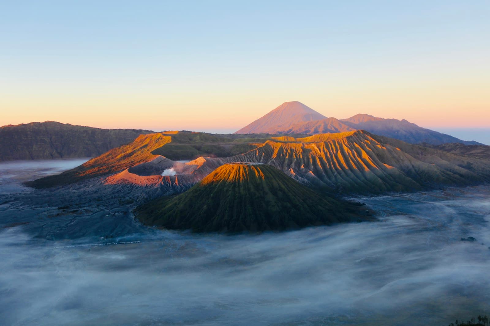 A steaming volcanic crater and ridgelines above a sea of cloud at sunrise