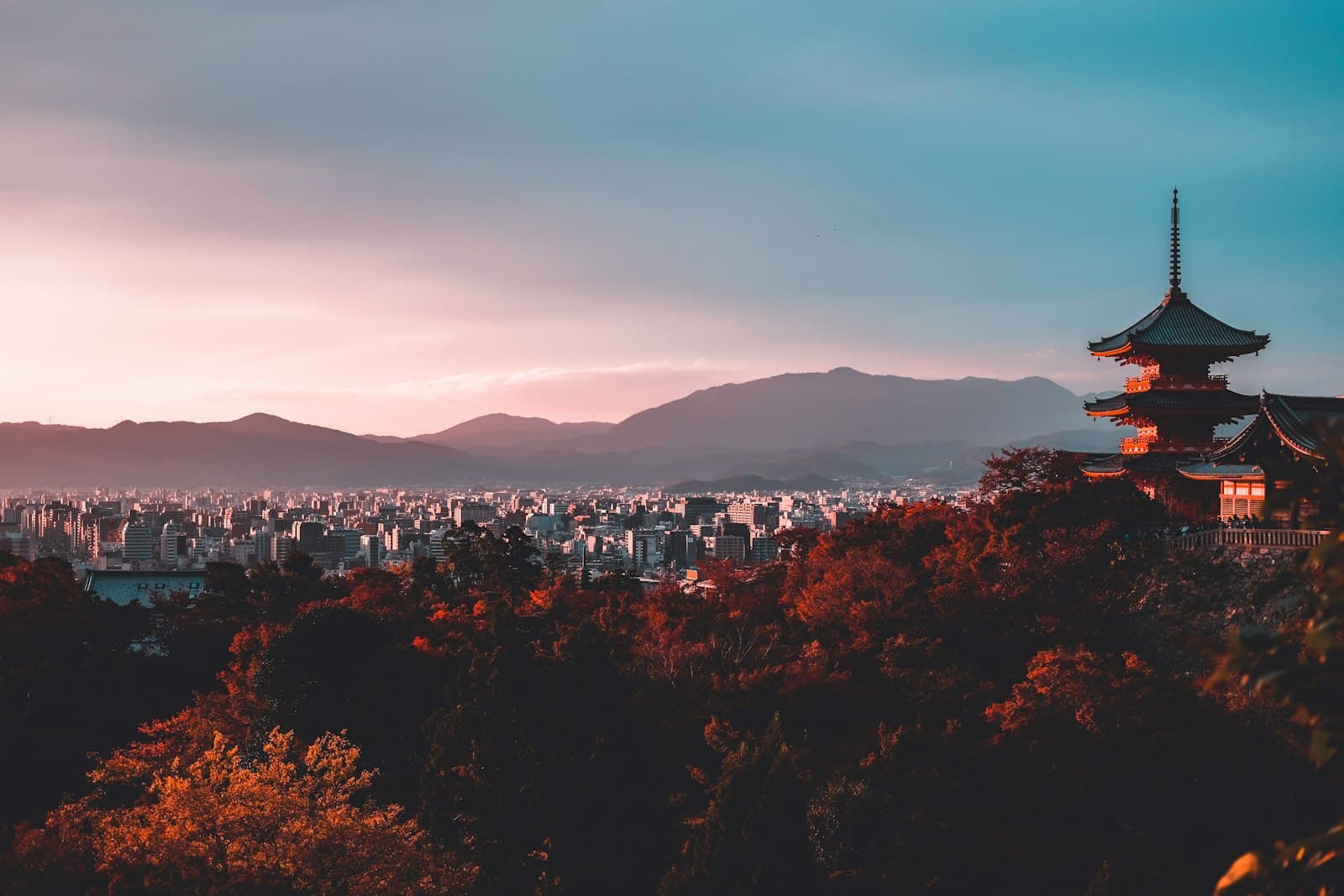 A wooden pagoda above autumn trees and the Kyoto cityscape at dusk