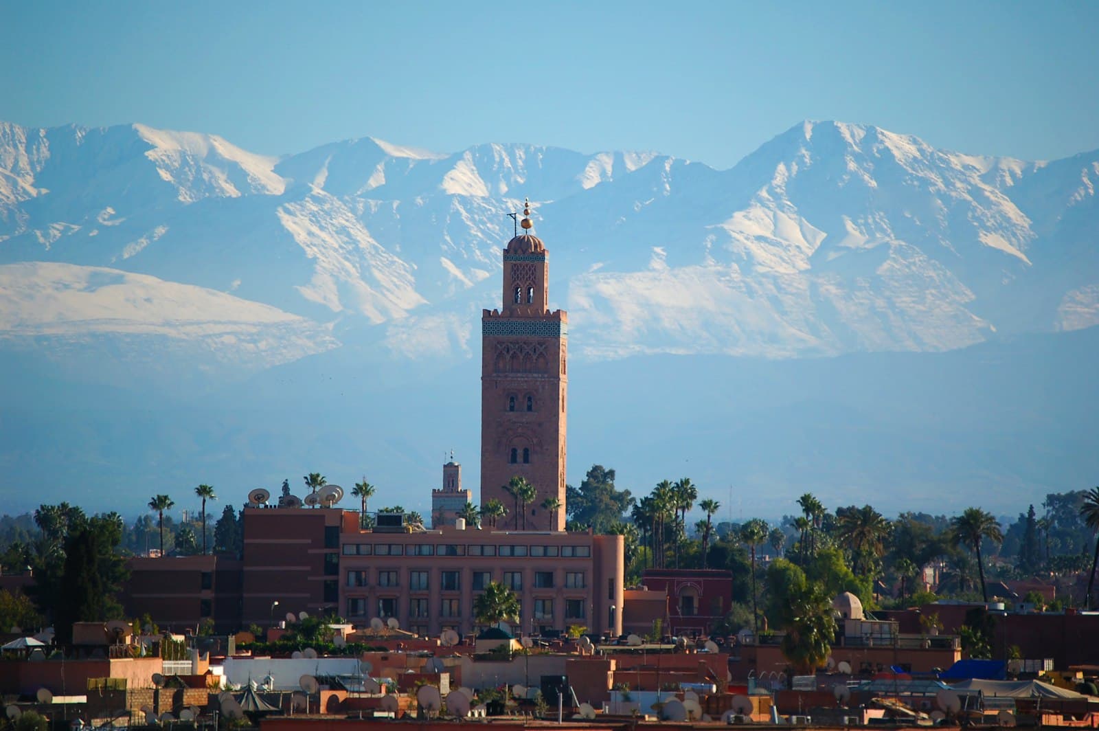 A minaret above Marrakech rooftops, with the snow-covered Atlas Mountains behind