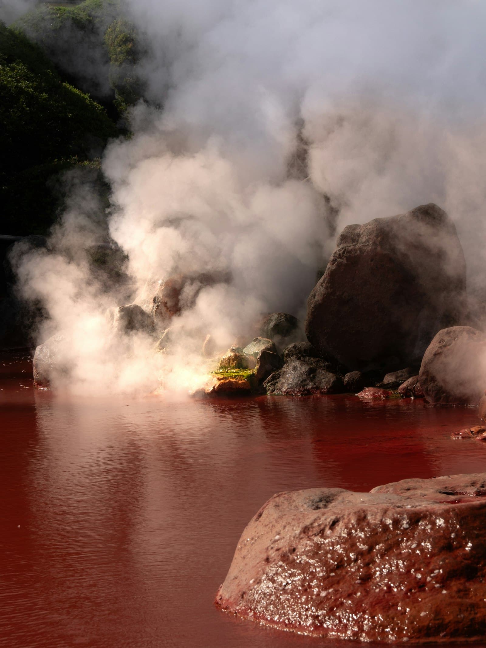 Steam rising from a red mineral hot-spring pool among rocks