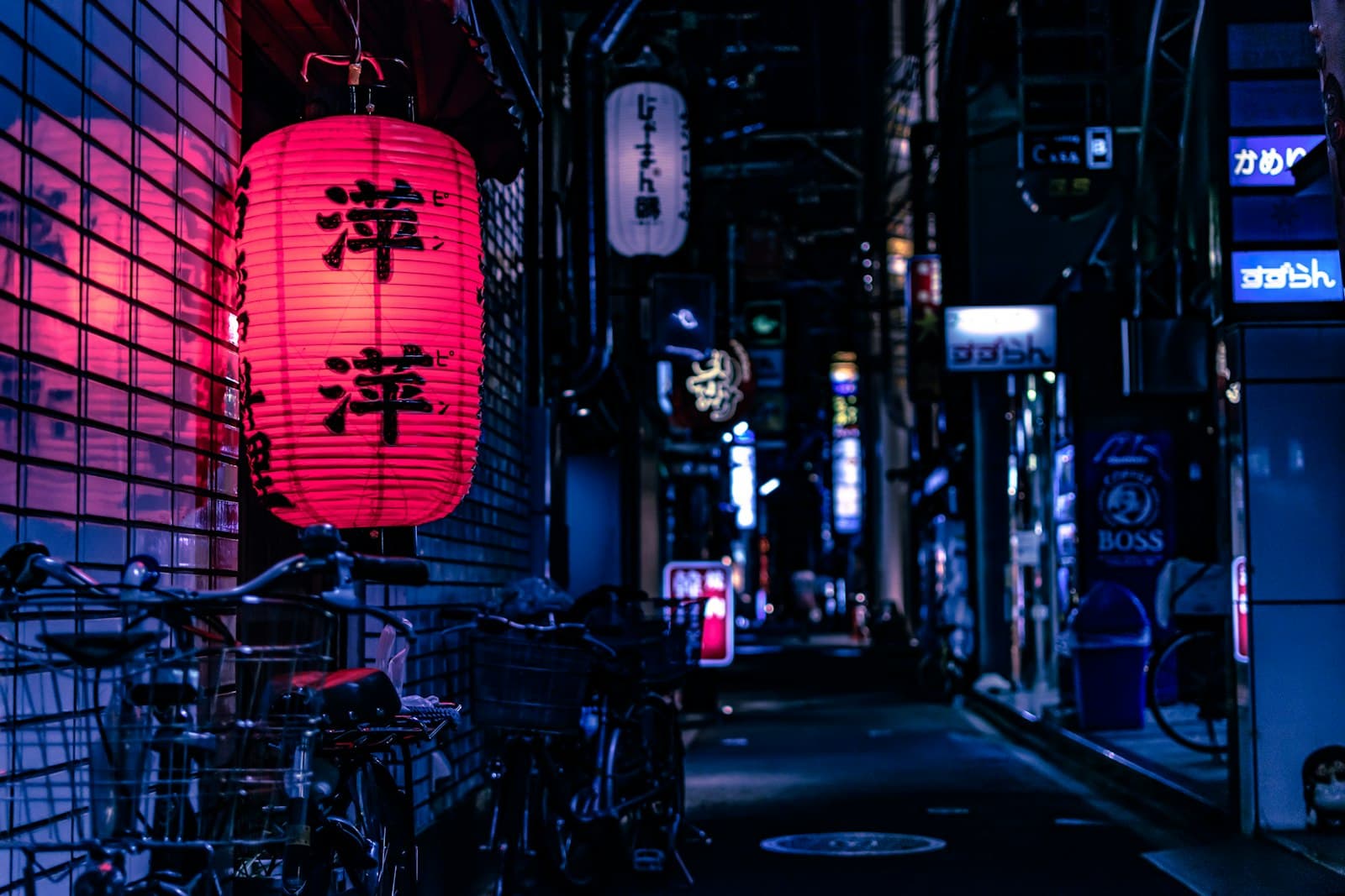 A red paper lantern lighting a narrow street of signs and parked bicycles at night