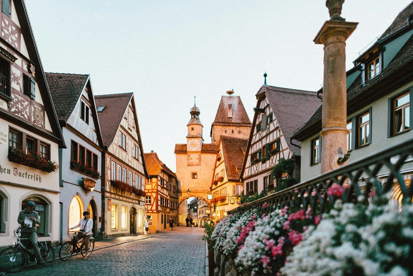 A flower-lined old town street leading toward a clock tower