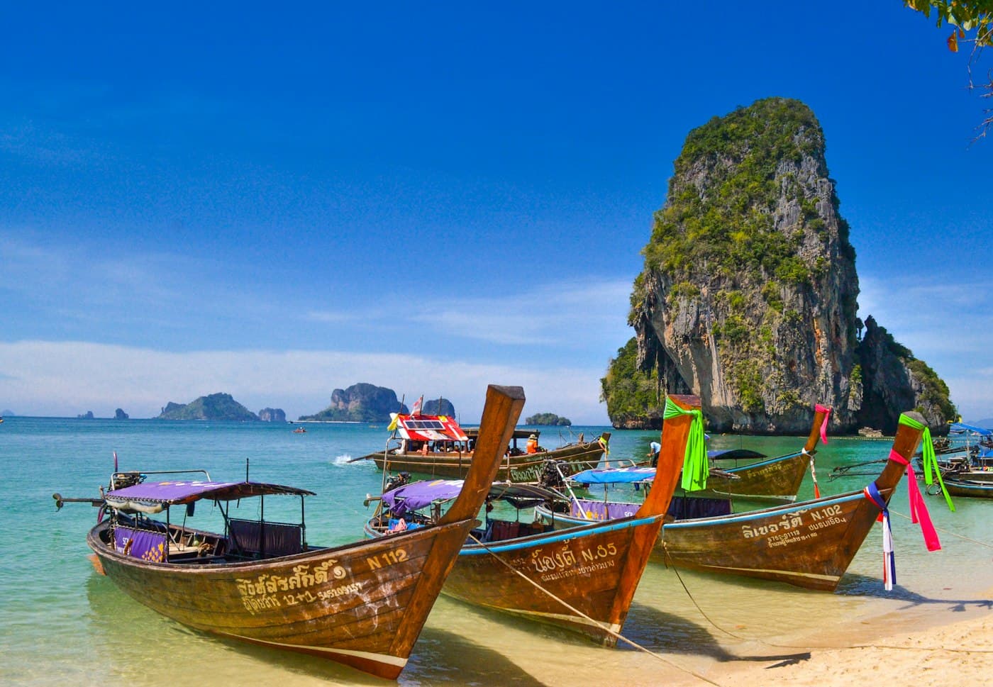 Long-tail boats on a beach beside a limestone island in Thailand